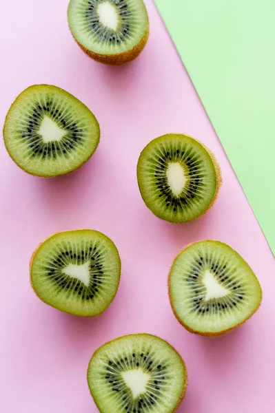 Вид зверху на половинки зі свіжими фруктами ківі на зеленому та рожевому — стокове фото