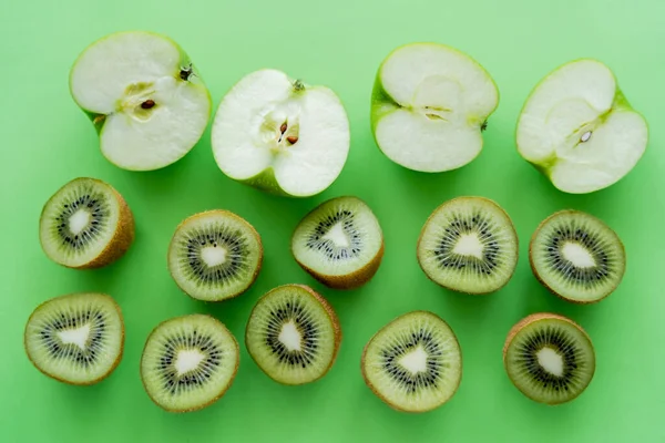 Puesta plana de manzanas y kiwis mitades de frutas en verde - foto de stock