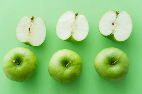 Disposición plana de sabrosas manzanas enteras y cortadas en verde - foto de stock