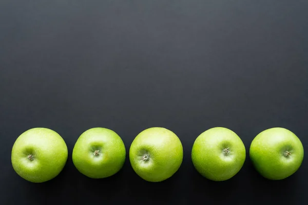 Vue de dessus des pommes fraîches et vertes en rangée sur noir — Photo de stock