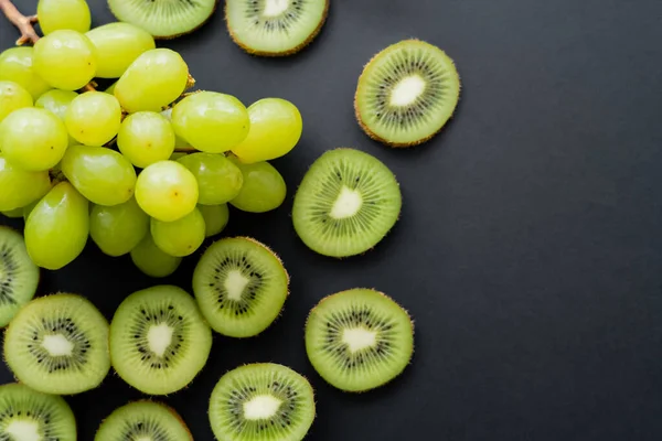 Top view of green ripe grapes and sliced kiwi on black — Fotografia de Stock