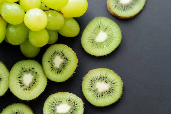 Vista superior de uvas verdes e kiwi fatiado em preto — Fotografia de Stock