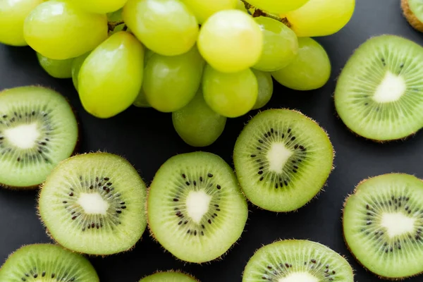 Vue de dessus des raisins verts et du kiwi frais tranché sur noir — Photo de stock