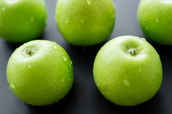 Close up view of green and juicy apples with water drops on black — стоковое фото