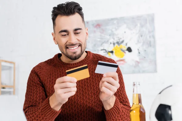 Smiling bookmaker holding credit cards near blurred soccer ball and beer — Photo de stock