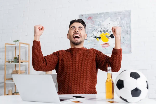 Overjoyed gambler showing win gesture near laptop, soccer ball and beer — Stockfoto
