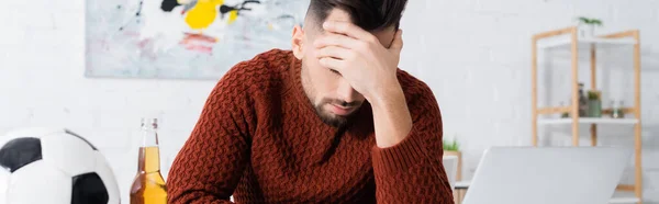 Upset gambler obscuring face near laptop, bottle of beer and soccer ball, banner — Stock Photo