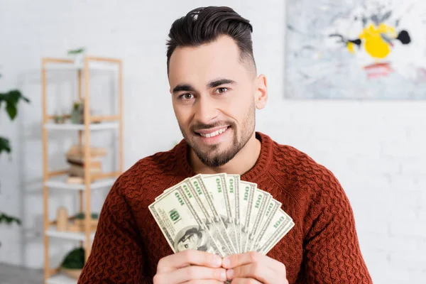 Bookmaker joyeux regardant la caméra et montrant des billets en dollars — Photo de stock