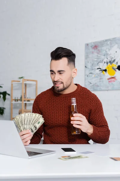 Joueur souriant avec des dollars et bouteille de bière près de l'ordinateur portable et smartphone avec écran vierge — Photo de stock