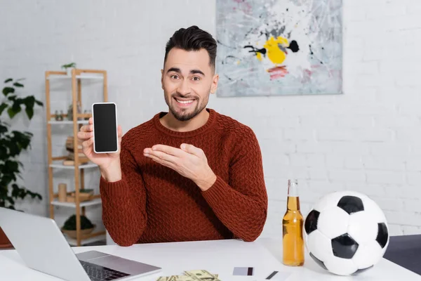 Cheerful gambler with soccer ball near credit cards and laptop with sports game on screen — Fotografia de Stock