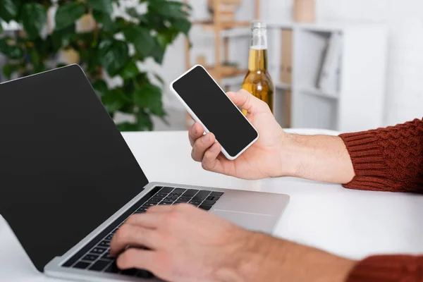Cropped view of gambler with smartphone typing on laptop with blank screen — Stock Photo