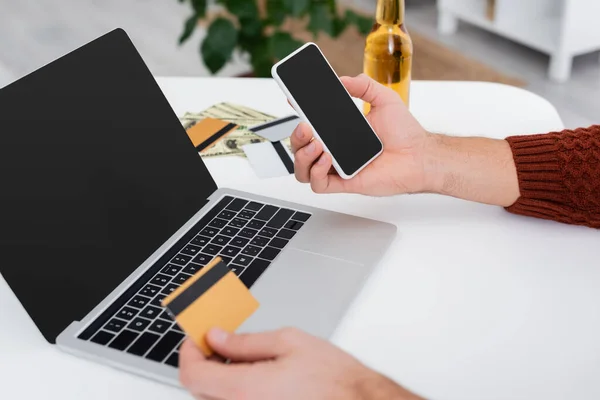 Обрезанный вид игрока с кредитной карты и мобильного телефона рядом с ноутбуком с пустым экраном — стоковое фото