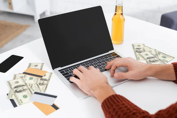 Partial view of gambler typing on laptop with blank screen near dollars and credit cards — Photo de stock