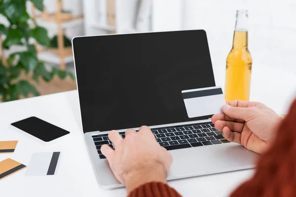 Partial view of bookmaker near laptop with blank screen, credit cards and beer — Stock Photo