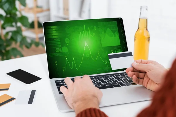 Partial view of bookmaker holding credit card near laptop with infographics on screen — Photo de stock