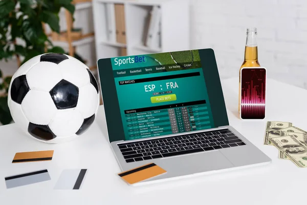 KYIV, UKRAINE - FEBRUARY 4, 2022: soccer ball, credit cards and dollars near smartphone with charts and laptop with sportsbet website — Stockfoto