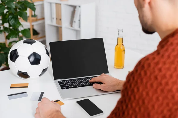 Cropped view of bookmaker near laptop with blank screen, soccer ball and credit cards - foto de stock