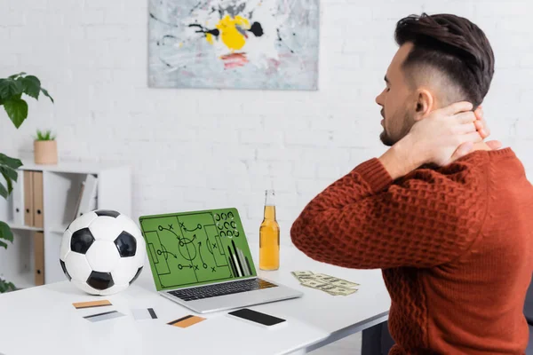 Upset bookmaker touching neck near credit cards and laptop with sports game strategy on screen — Foto stock