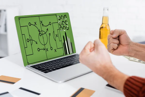 Vista recortada de corredor de apuestas que muestra el gesto de éxito cerca de la computadora portátil con estrategia de juego de deportes en la pantalla - foto de stock