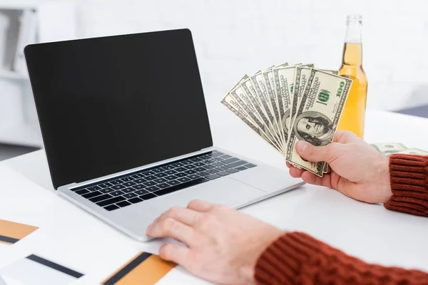 Partial view of bookmaker with dollar banknotes near laptop with blank screen - foto de stock