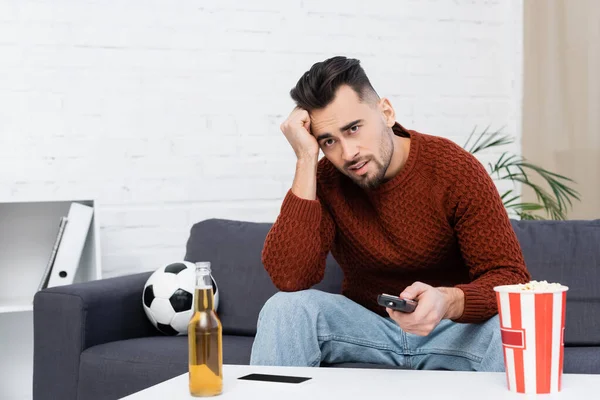 Chateado fã de esportes assistindo campeonato na tv perto de bola de futebol e garrafa de cerveja — Fotografia de Stock