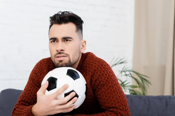 Ventilador de esportes preocupado com bola de futebol assistindo campeonato em casa — Fotografia de Stock