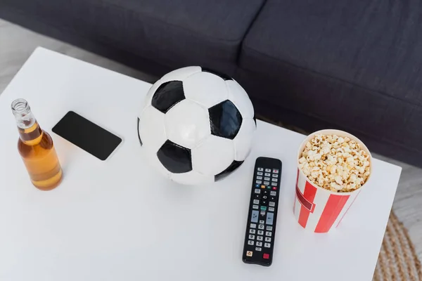 Vista ad alto angolo di pallone da calcio, popcorn, telecomando TV e telefono cellulare sul tavolo — Foto stock