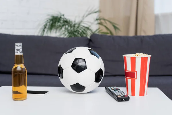 Soccer ball, bucket of popcorn, tv remote controller, beer and smartphone on table — Stock Photo