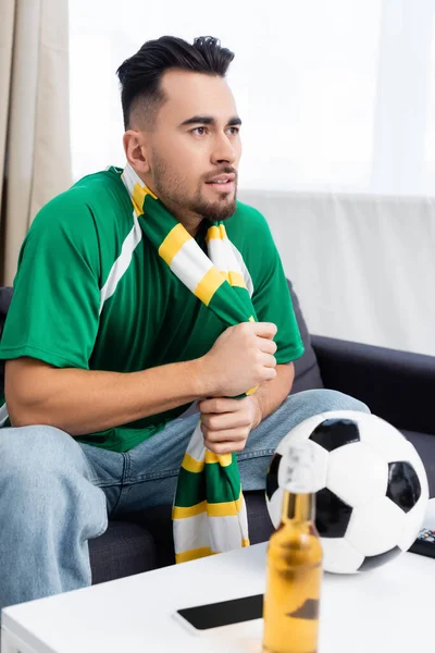 Deporte concentrado ventilador viendo campeonato en casa cerca de pelota de fútbol y botella de cerveza - foto de stock