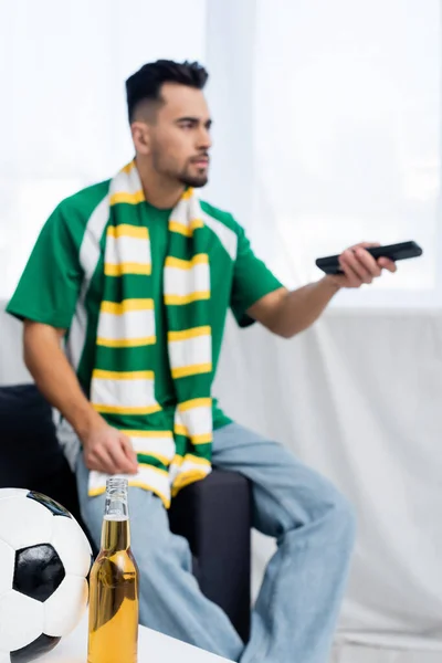 Selective focus of soccer ball and beer near blurred sports fan clicking tv channels — Photo de stock