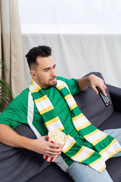 Concentrated sports fan with tv remote controller and popcorn watching game at home — Stock Photo