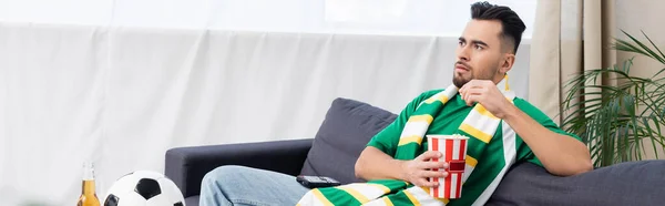 Sports fan eating popcorn while watching game on tv near soccer ball, banner — Stock Photo