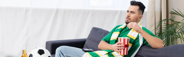 Sports fan eating popcorn while watching game on tv near soccer ball, banner — Fotografia de Stock