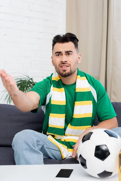 Displeased sports fan pointing with hand while watching football match on tv at home — Stock Photo