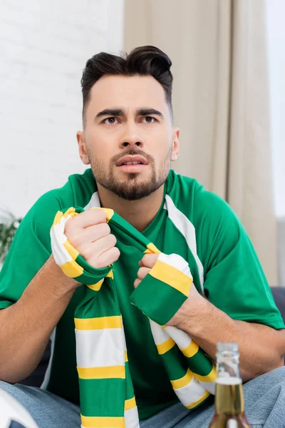 Worried sports fan in striped scarf watching championship at home — Photo de stock