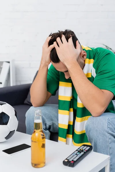 Frustrated sports fan sitting with bowed head near soccer ball and beer — Photo de stock