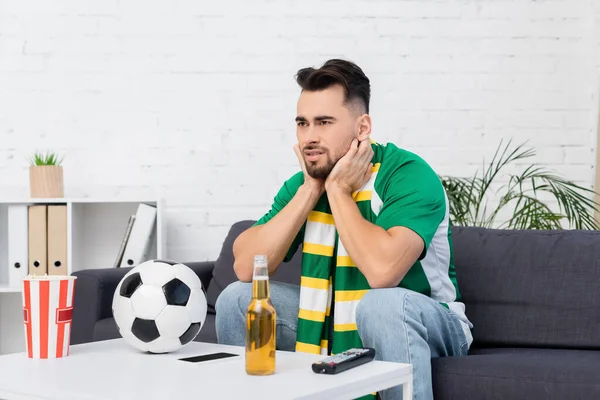 Worried sports fan watching championship near soccer ball and beer at home — Fotografia de Stock