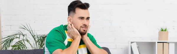 Fanático de los deportes tensos en bufanda rayada viendo el campeonato en casa, bandera - foto de stock