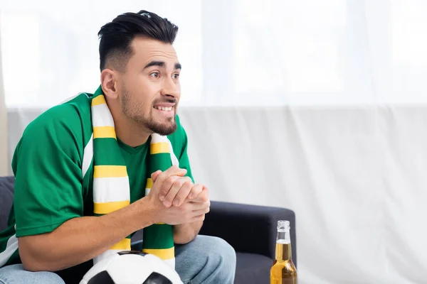 Homem preocupado com as mãos apertadas assistindo jogo na tv perto de bola de futebol e cerveja — Fotografia de Stock