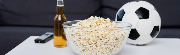 Bowl of popcorn near bottle of beer, tv remote controller and soccer ball on table, banner — Fotografia de Stock