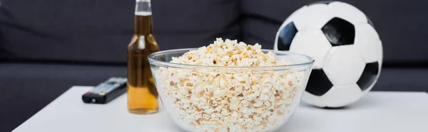Bowl of popcorn near bottle of beer, tv remote controller and soccer ball on table, banner — Foto stock