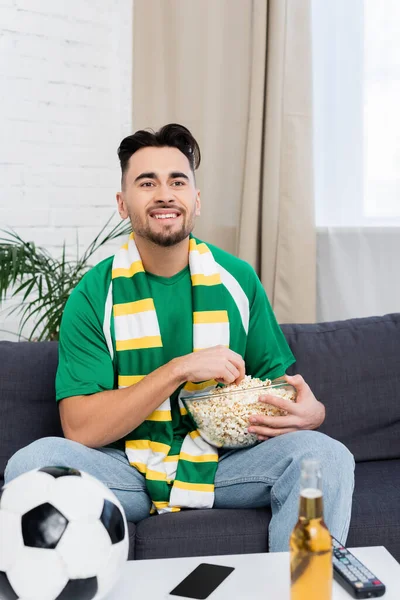 Happy football fan with bowl of popcorn watching match on tv at home — Photo de stock