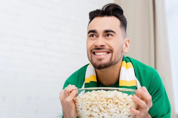 Thrilled sports fan holding bowl of popcorn while watching championship at home — Stock Photo