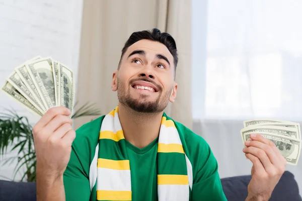 Happy gambler looking up while holding dollars and bottle of beer — Stock Photo