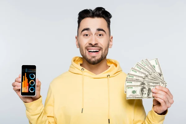 Happy bookmaker with dollars showing smartphone with analytics isolated on grey — Stock Photo
