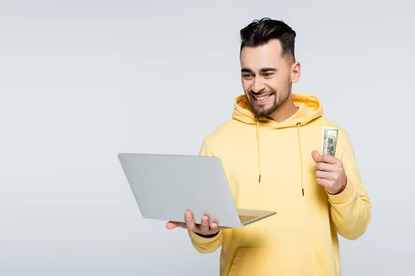 Happy gambler holding dollars and laptop isolated on grey — Stock Photo