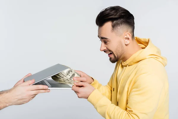 Visão lateral do jogador animado segurando dinheiro perto de laptop isolado em cinza — Fotografia de Stock
