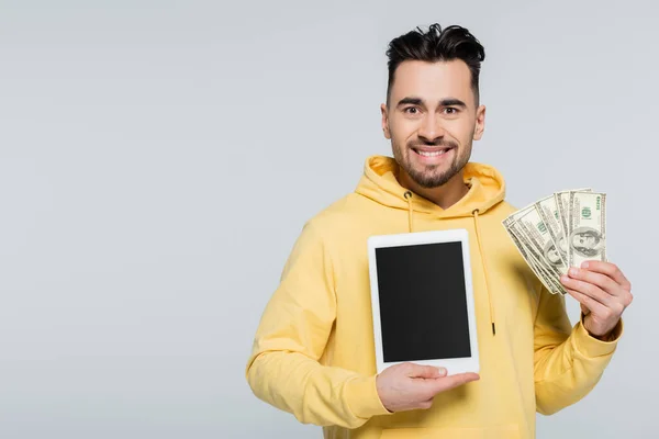 Joyful gambler holding dollars and digital tablet with blank screen isolated on grey — Stock Photo