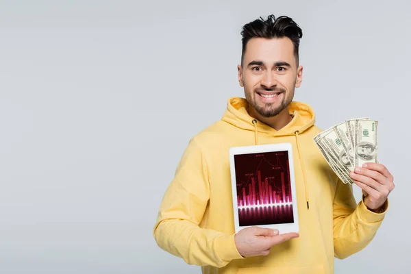 Casa de apuestas sonriente sosteniendo dólares y tableta digital con analítica aislada en gris - foto de stock