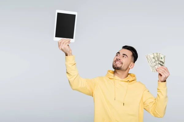 Cheerful bookmaker holding money and digital tablet with blank screen isolated on grey — Stock Photo